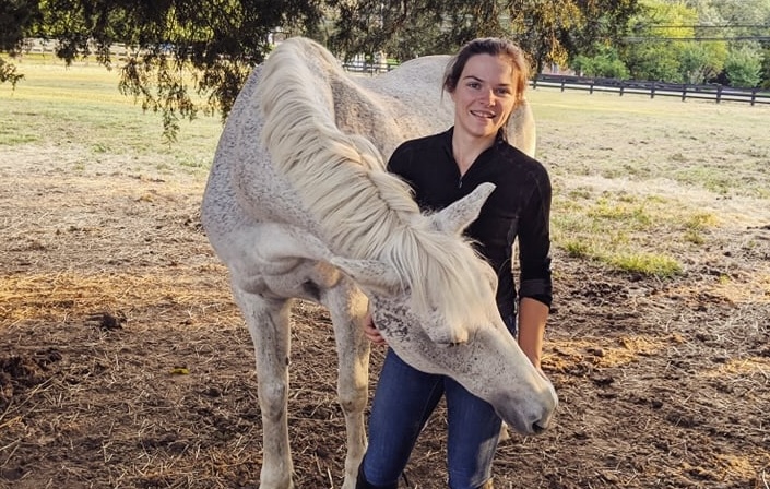 Abigail stands beside a gray horse, who is nuzzling her arm.
